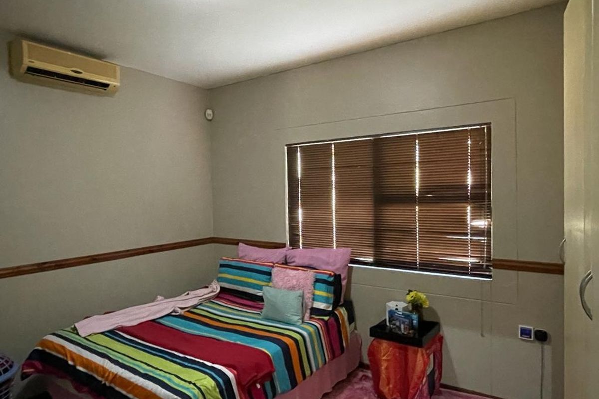 A bedroom featuring a wall-mounted air conditioning unit, built-in wardrobe, and window with fitted blinds.
