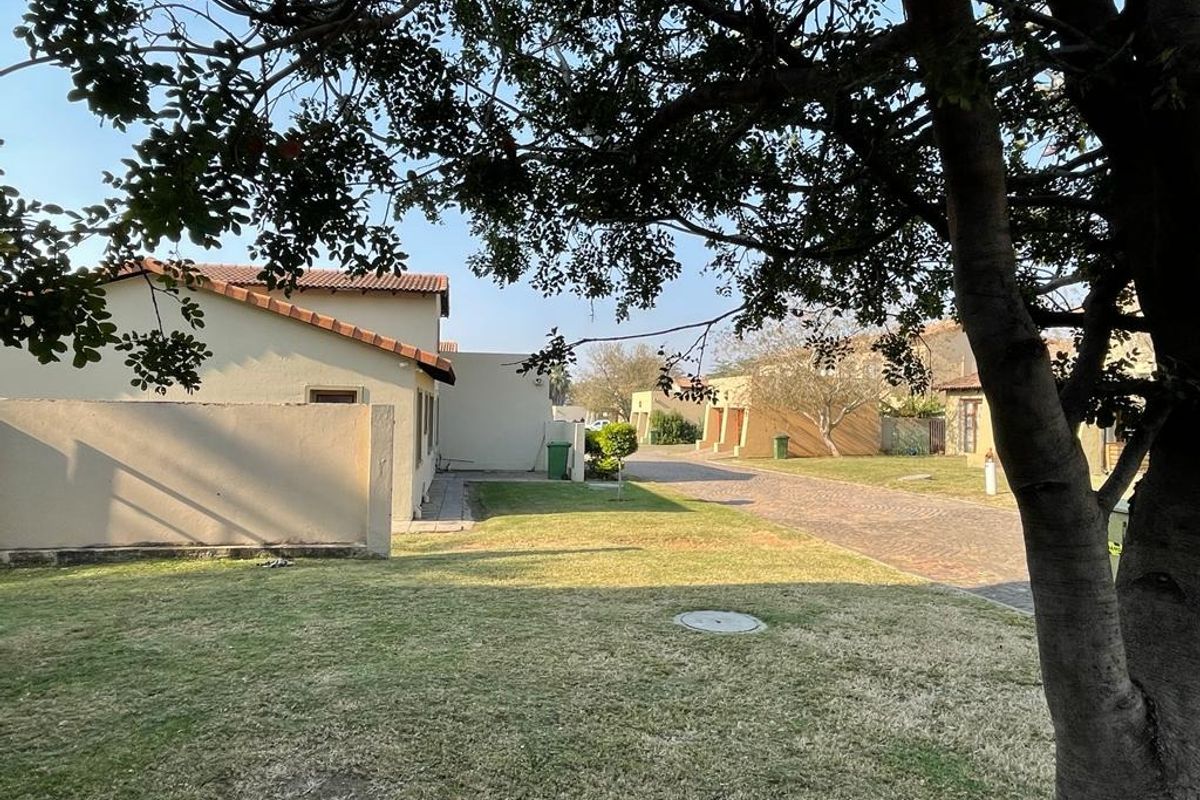 A view of the property exterior showing the garden, paved driveway, and surrounding residential structures under a clear sky.