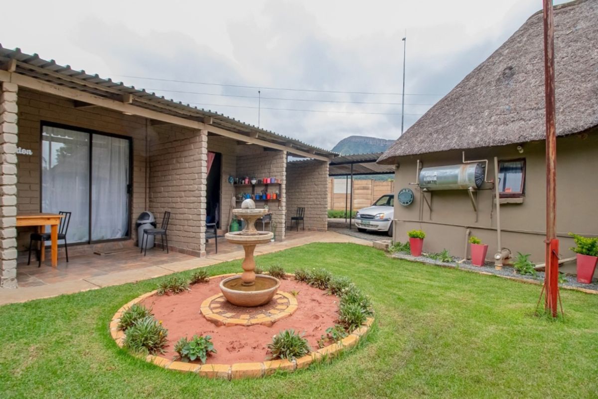 A rear garden area featuring a central stone fountain, a covered patio with brick pillars, and a thatched-roof structure with an external geyser.
