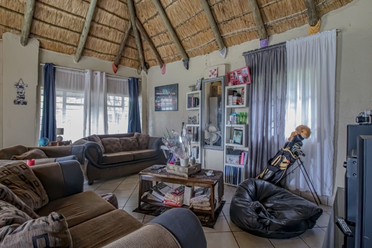 A living room featuring a traditional thatched roof, tiled flooring, and large windows allowing for natural light.