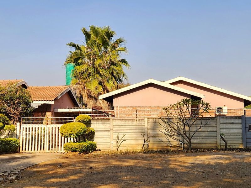 Exterior view of the townhouse complex featuring a paved driveway, perimeter boundary wall, and established garden landscaping.