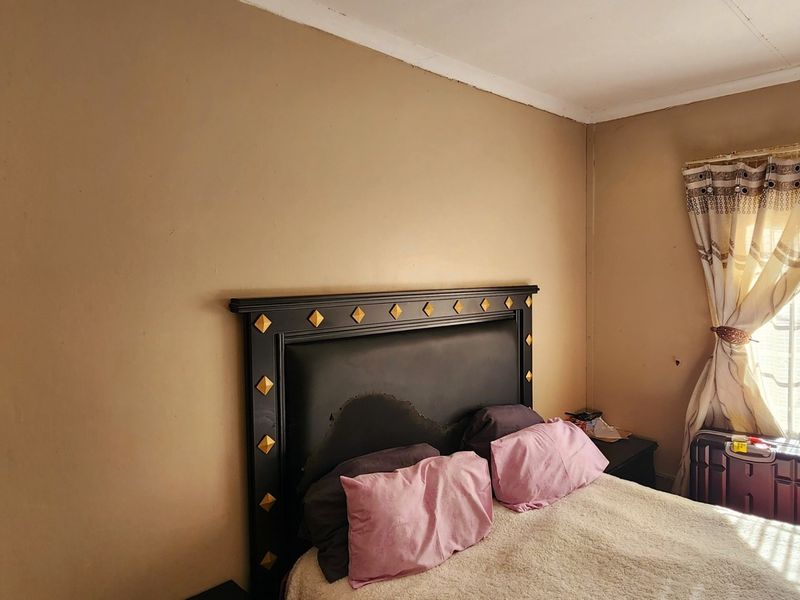 A bedroom featuring a dark headboard, neutral wall tones, and natural light through a window with curtains.