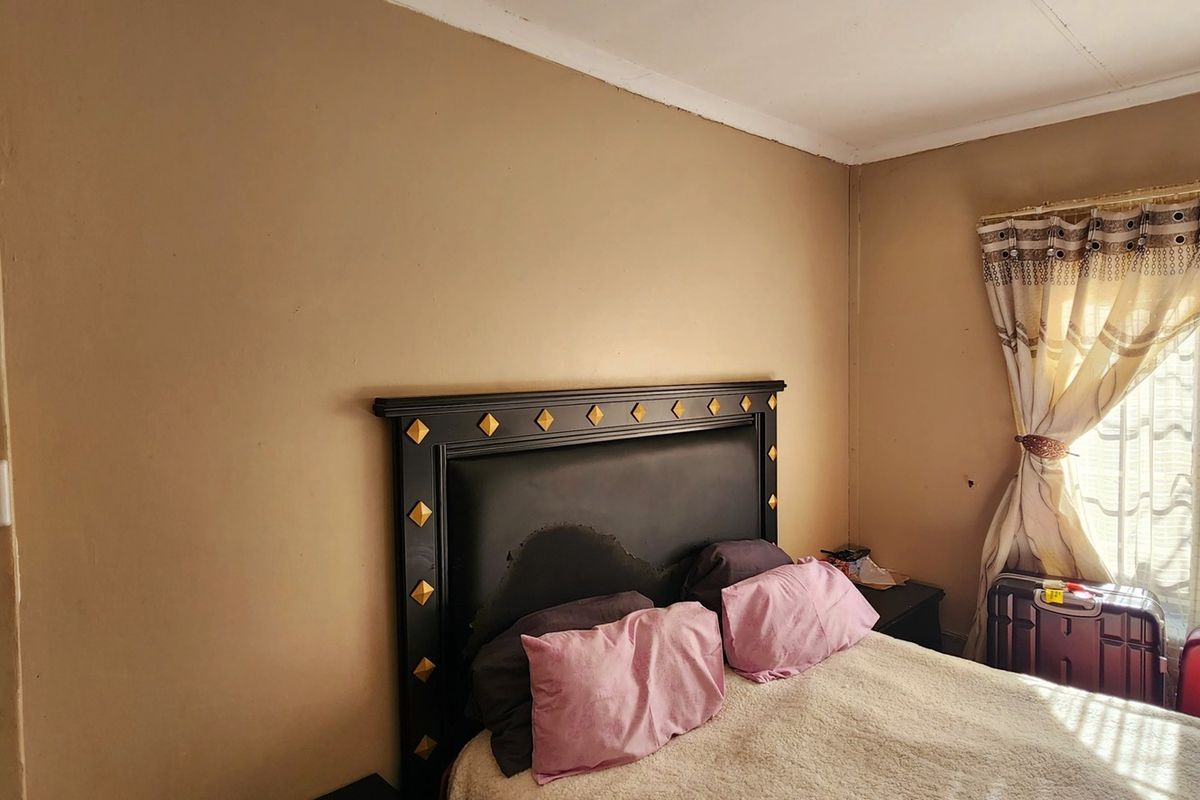 A bedroom featuring a dark headboard, neutral wall tones, and natural light through a window with curtains.