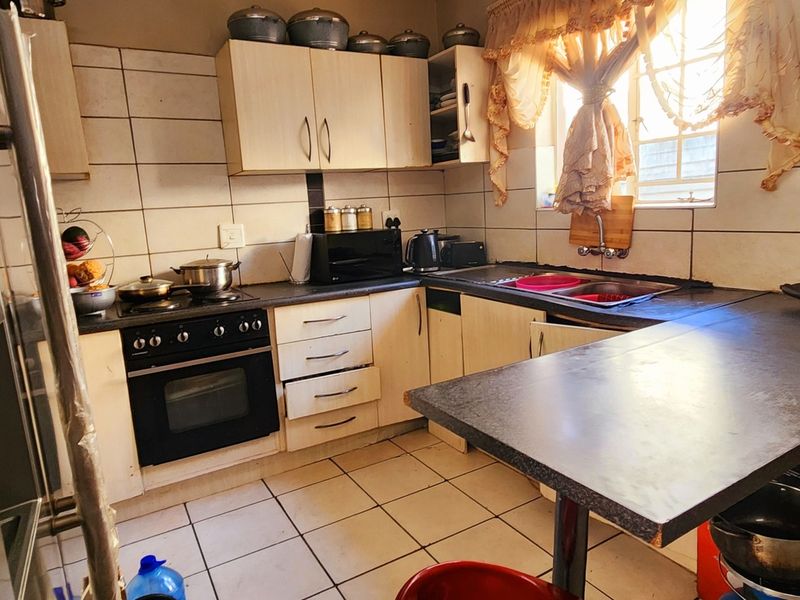 A functional kitchen featuring built-in cabinetry, a stove with oven, double sink, and tiled flooring with a breakfast counter.