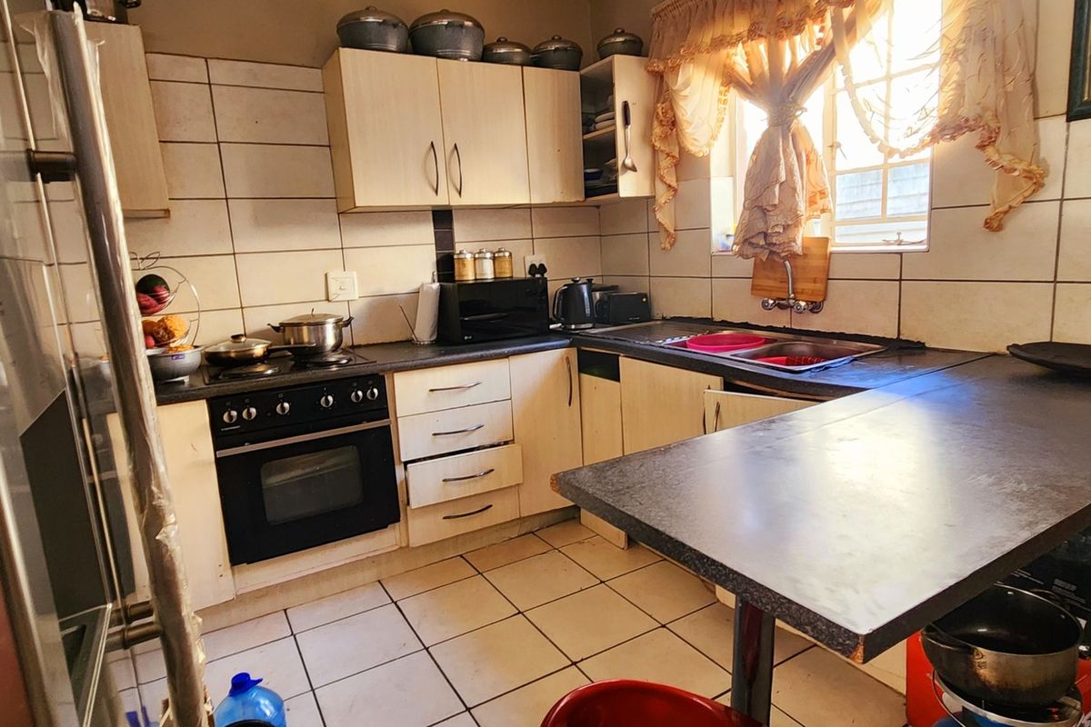 A functional kitchen featuring built-in cabinetry, a stove with oven, double sink, and tiled flooring with a breakfast counter.