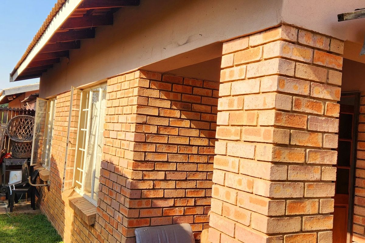 A view of the rear exterior of the townhouse, featuring exposed brick pillars, a covered patio area, and a small garden space.