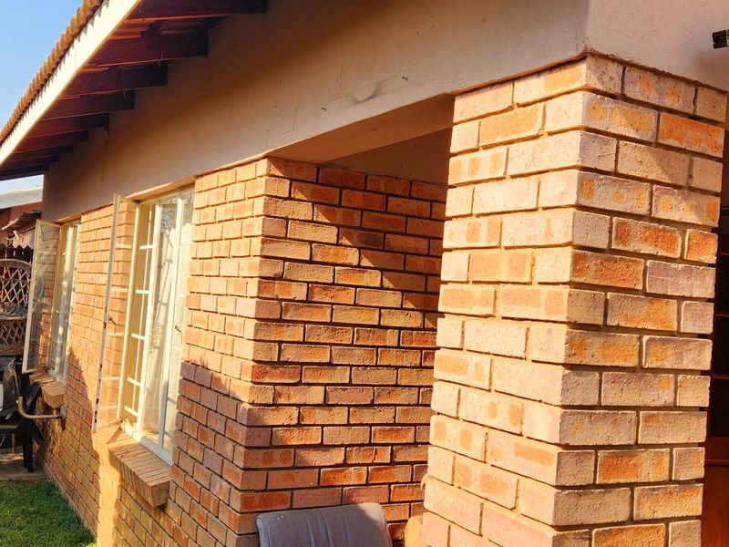 A view of the rear exterior of the townhouse, featuring exposed brick pillars, a covered patio area, and a small garden space.