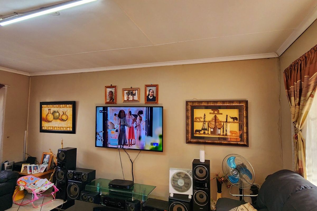 A living room featuring tiled flooring, large windows with curtain treatments, and a central wall-mounted television setup.