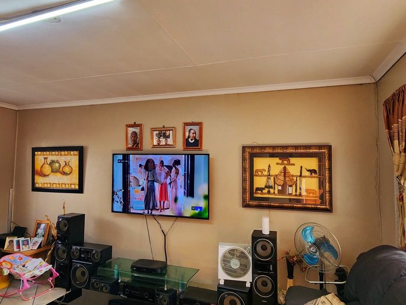 A living room featuring tiled flooring, large windows with curtain treatments, and a central wall-mounted television setup.