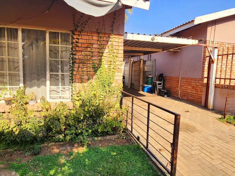 Exterior view of a townhouse featuring a brick facade, paved driveway, and a covered carport area with adjacent garden space.