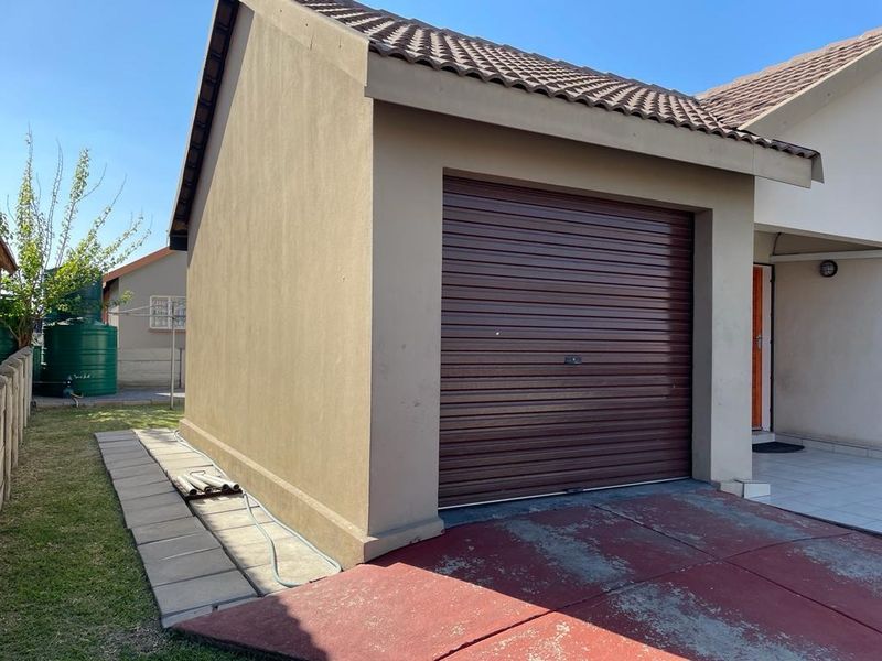 A single garage with a brown roll-up door and tiled roof, featuring a paved walkway and a concrete driveway.
