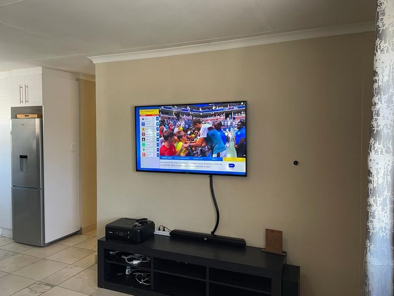 A living area featuring tiled flooring and coved ceilings, with a wall-mounted television setup.