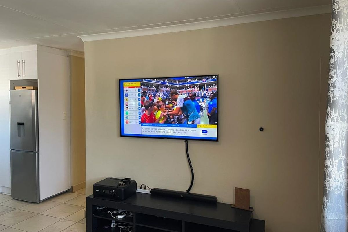 A living area featuring tiled flooring and coved ceilings, with a wall-mounted television setup.
