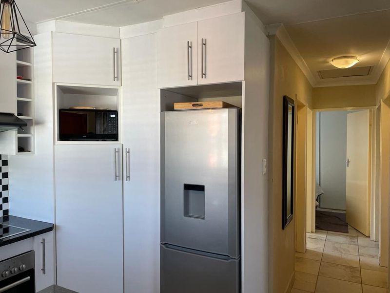 A functional kitchen featuring white built-in cabinetry, integrated appliances including an oven and hob, and tiled flooring, leading into a hallway.