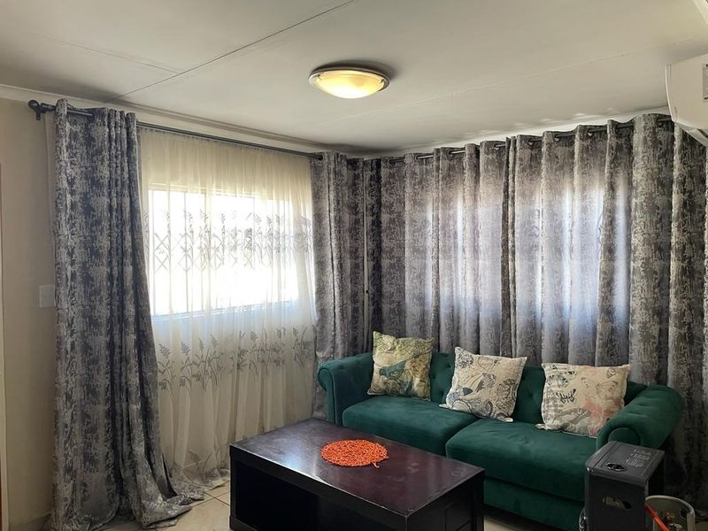 A living room featuring tiled flooring, air conditioning, and large windows fitted with security bars and floor-to-ceiling curtains.