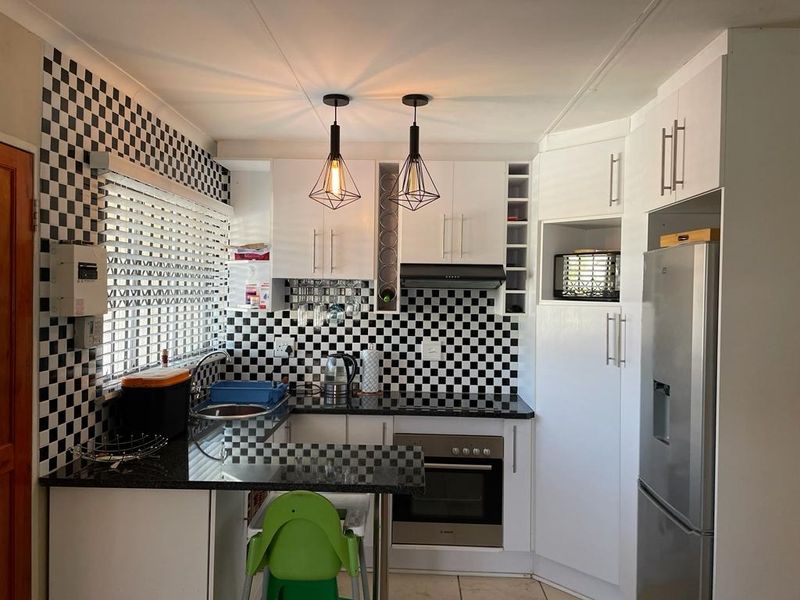 A compact, modern kitchen featuring white cabinetry, granite countertops, a stainless steel oven, and a distinctive black and white checkered tile backsplash.
