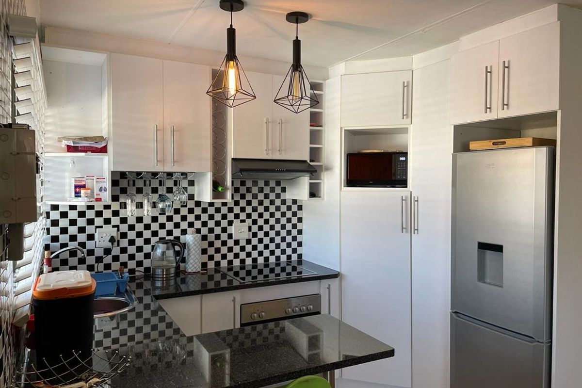 Modern kitchen featuring white cabinetry, black granite countertops, a distinctive checkerboard tile backsplash, and integrated appliances with stylish pendant lighting.