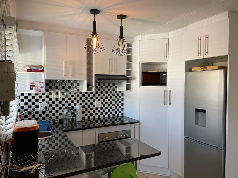 Modern kitchen featuring white cabinetry, black granite countertops, a distinctive checkerboard tile backsplash, and integrated appliances with stylish pendant lighting.
