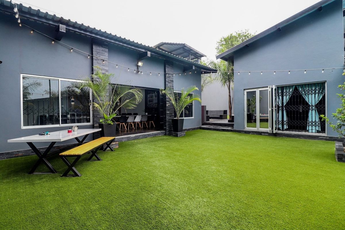 A well-maintained rear courtyard featuring artificial turf, modern dark-painted exterior walls, and integrated patio areas with string lighting.