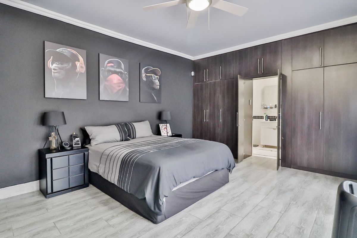 Spacious bedroom featuring dark grey accent walls, extensive built-in floor-to-ceiling cabinetry, light wood-look flooring, and an en-suite bathroom access.