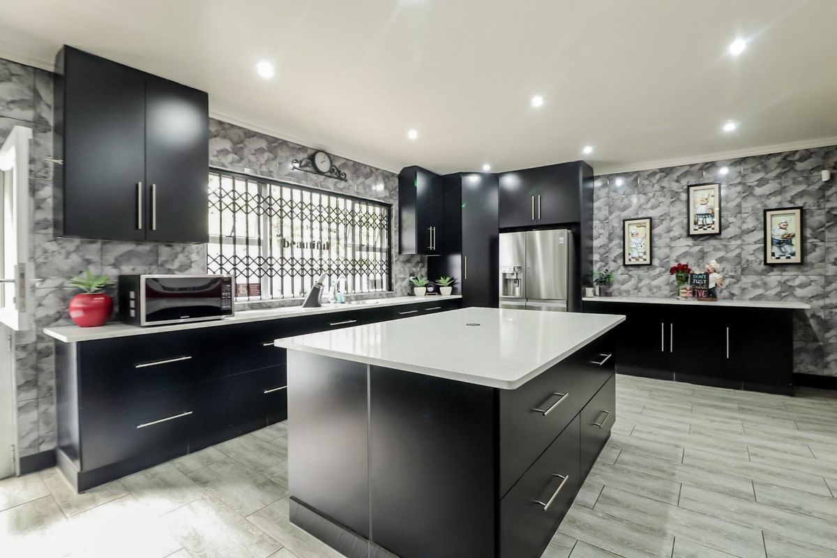 Modern kitchen featuring sleek black cabinetry, a central island with stone countertop, marble-effect wall tiling, and recessed ceiling lighting.