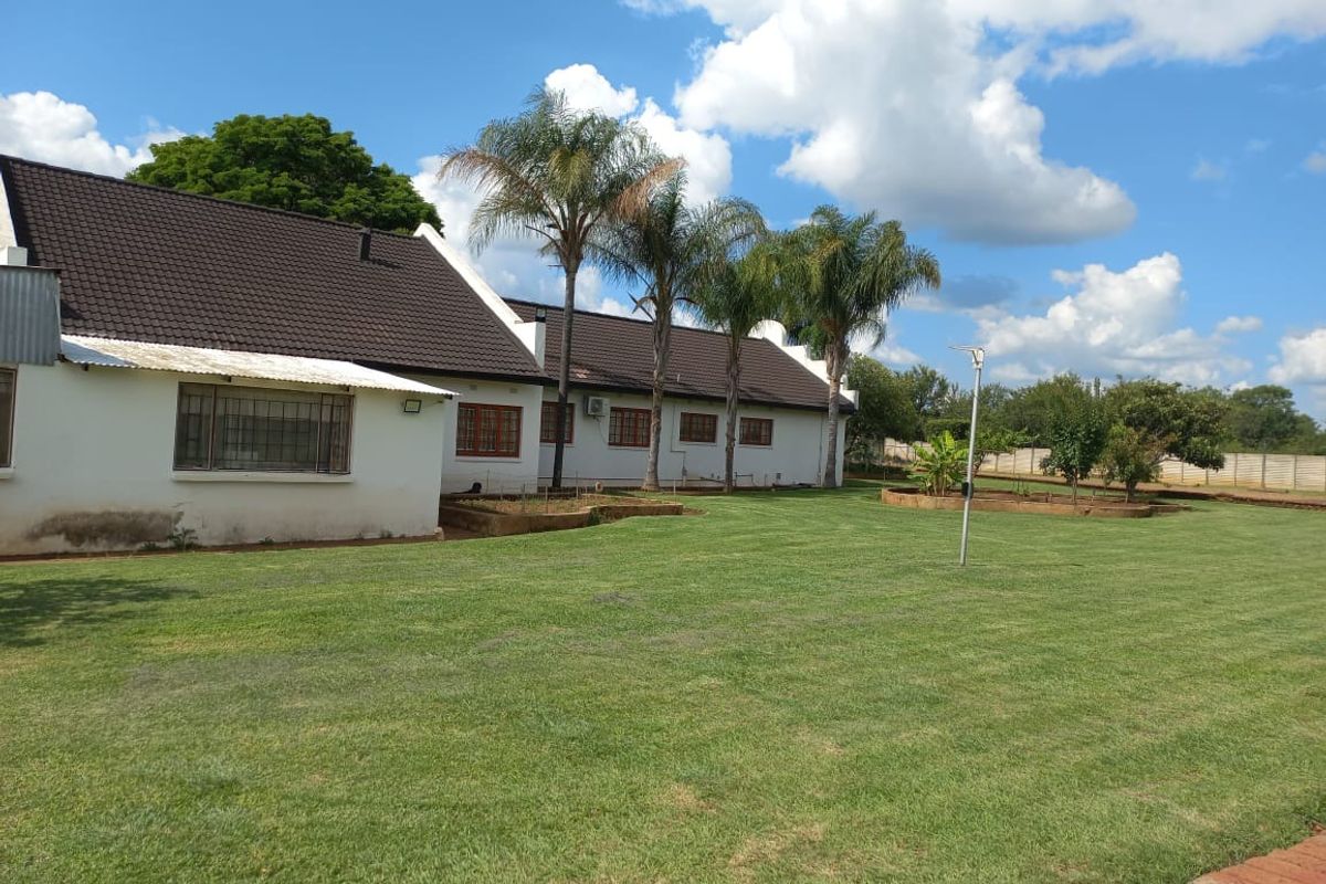 A view of the rear exterior of the farm property, featuring a well-maintained lawn, mature palm trees, and a white building with a dark tiled roof.