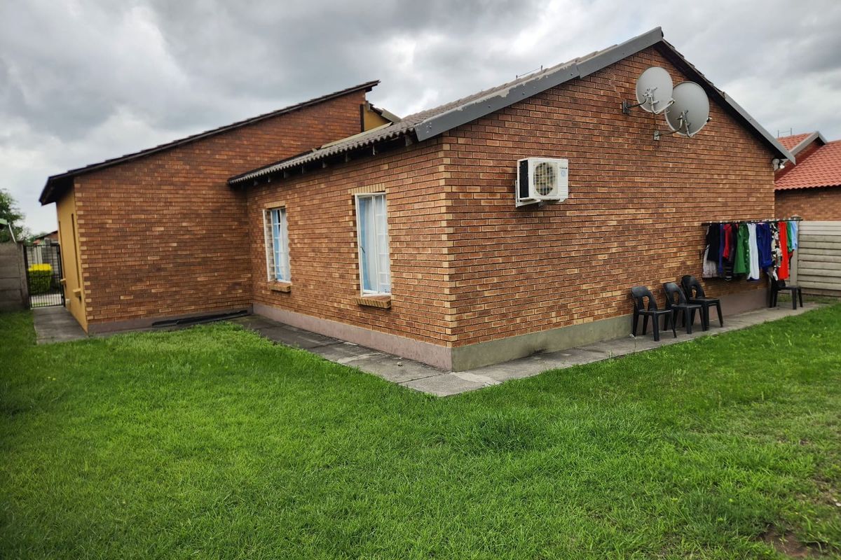 Rear exterior view of a face-brick house featuring a lawn, paved perimeter, wall-mounted air conditioning unit, and satellite dishes.