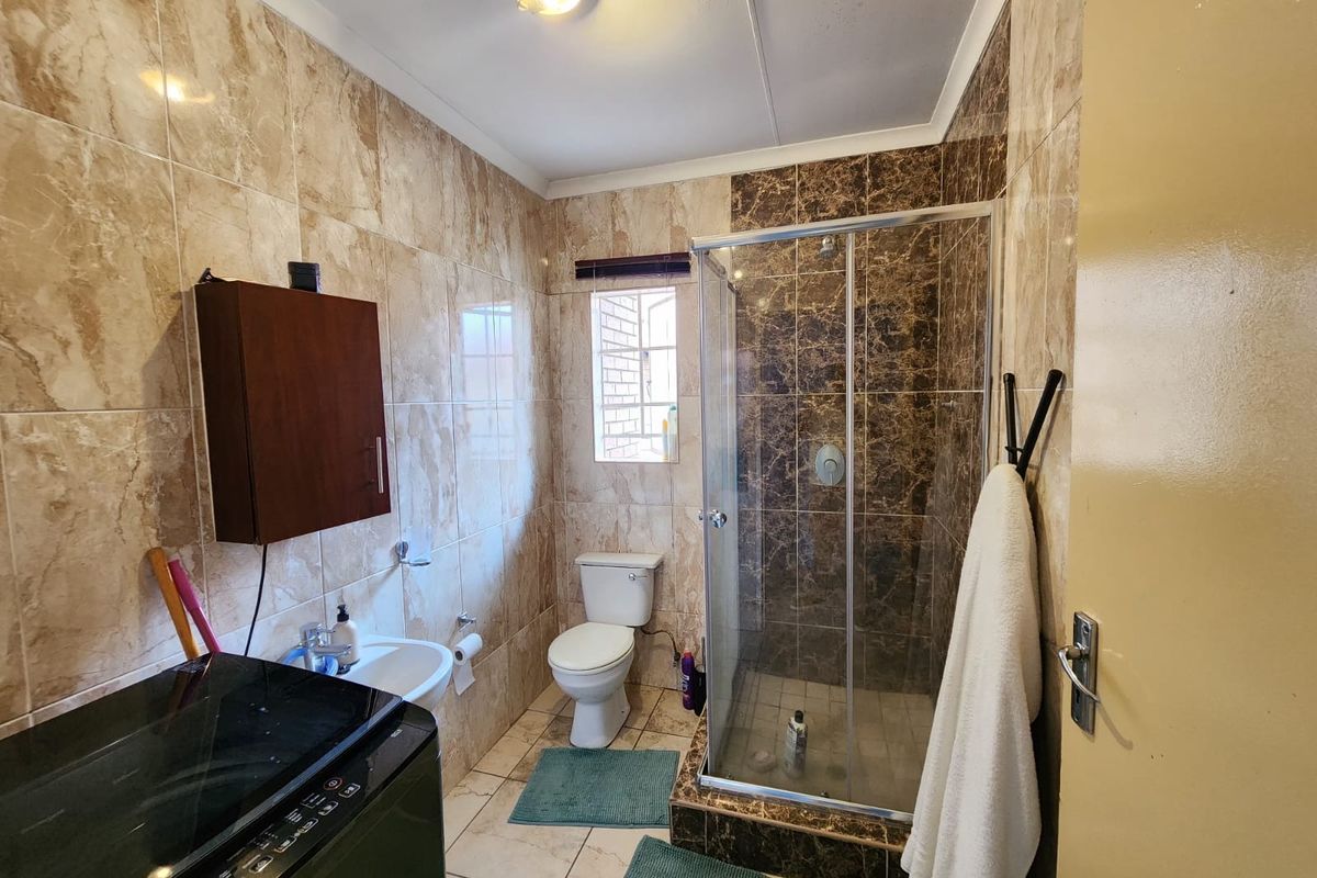 A functional bathroom featuring a glass-enclosed shower, toilet, and pedestal basin with full-height marble-effect wall tiling.