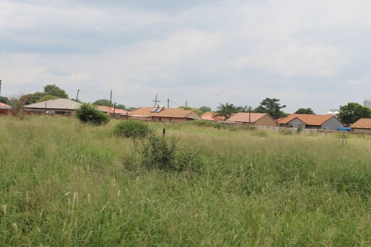 A view of an undeveloped residential plot of land with surrounding established housing in the background.