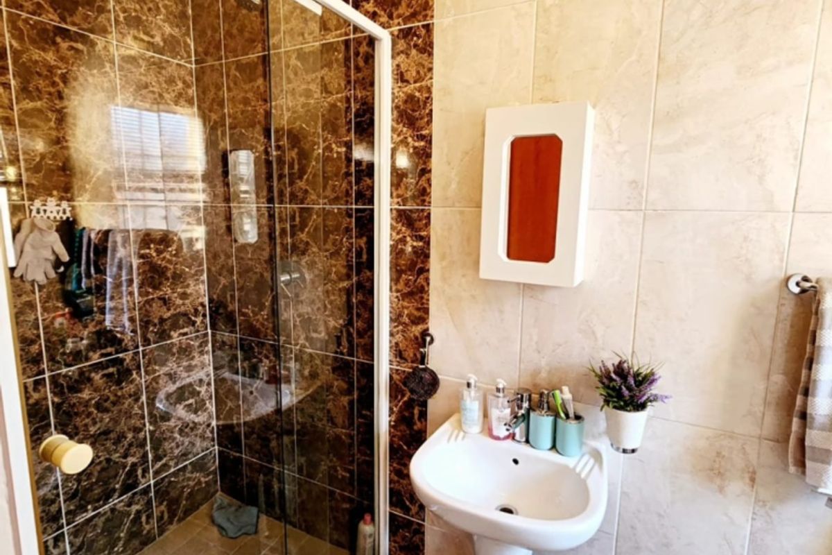 A bathroom featuring a glass-enclosed shower with dark marble-effect tiling and a white pedestal basin with wall-mounted storage.