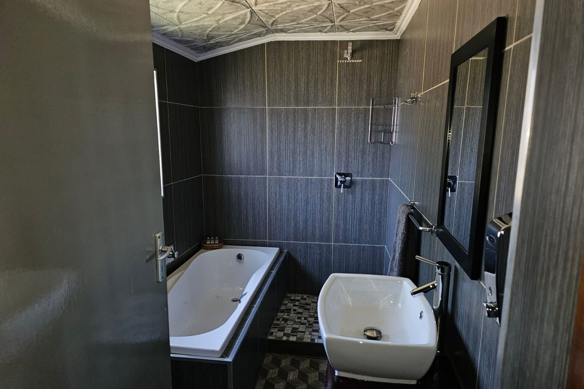 Compact bathroom featuring a built-in bathtub, modern vessel sink, wall-mounted shower head, and dark textured wall tiling.