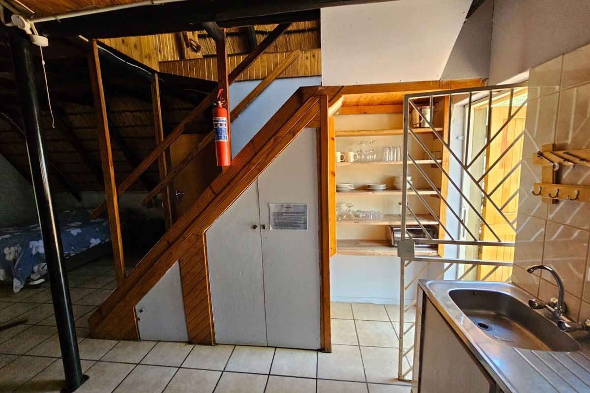 A rustic kitchen area featuring built-in timber shelving, a stainless steel sink, and an integrated staircase leading to an upper level.