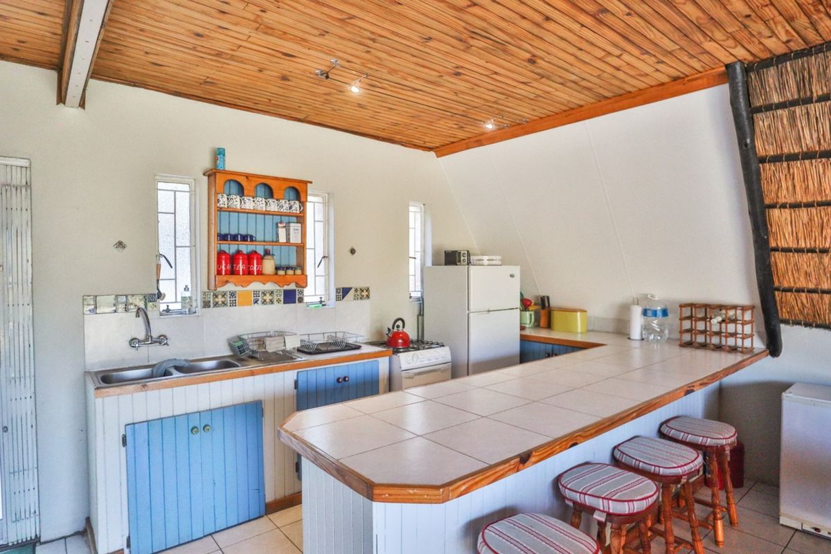 A rustic kitchen featuring a breakfast bar, tiled countertops, wooden ceiling, and blue cabinetry, offering a functional layout with integrated sink and stove.
