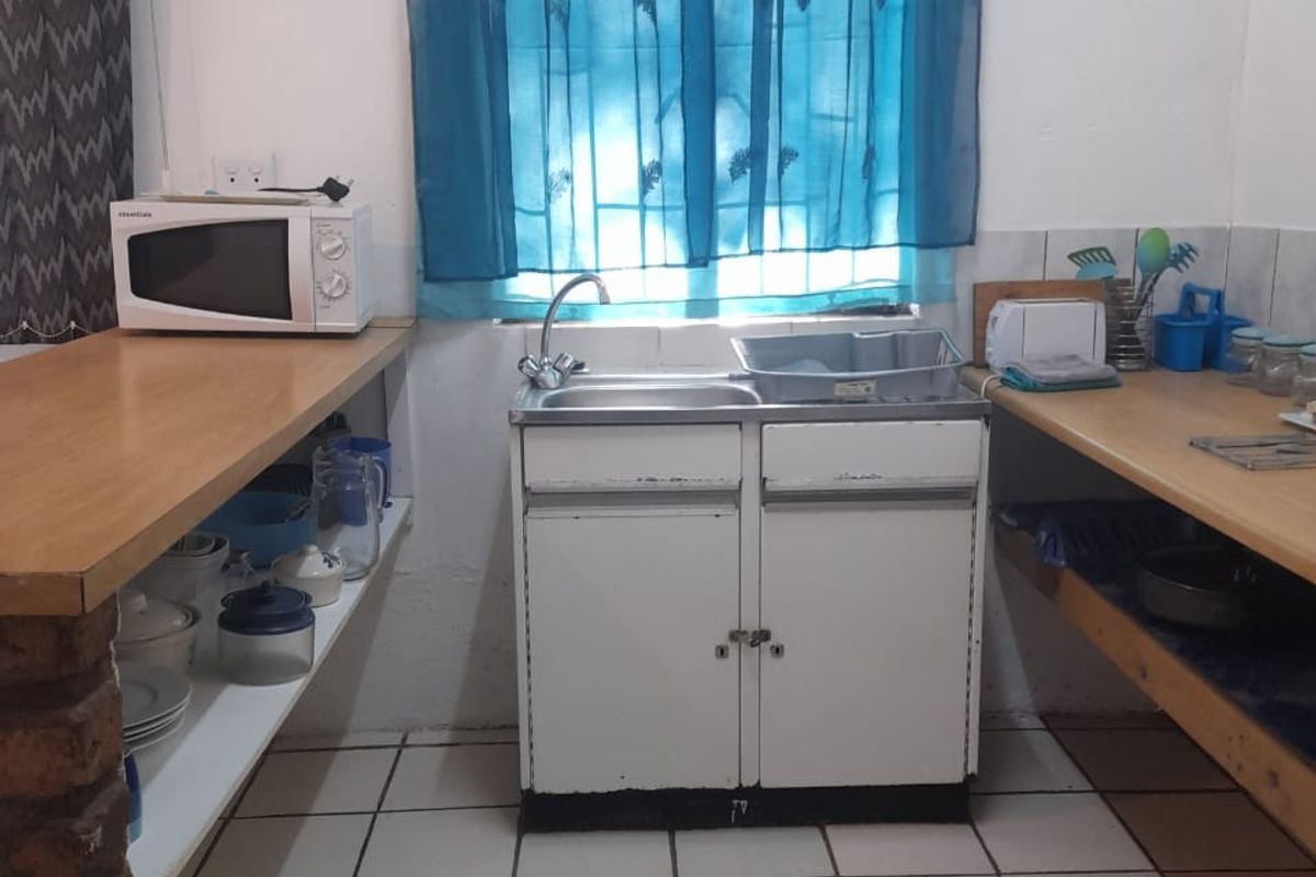 A functional kitchen area featuring a single sink unit, open shelving, and wooden countertops with tiled flooring.