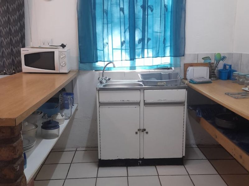 A functional kitchen area featuring a single sink unit, open shelving, and wooden countertops with tiled flooring.