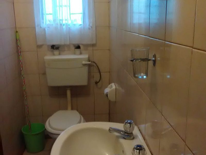 A compact bathroom featuring a standard toilet, wall-mounted basin with dual taps, and full-height wall tiling.