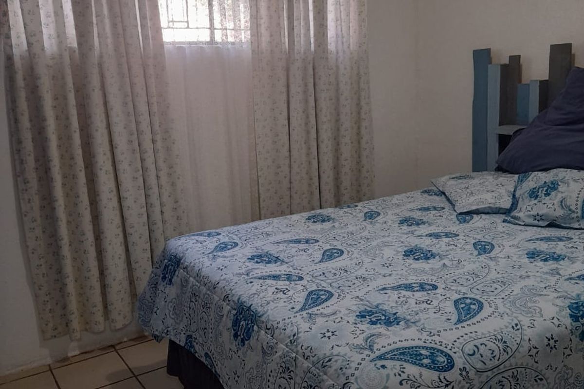 A functional bedroom featuring tiled flooring, a window with security bars, and neutral wall finishes.