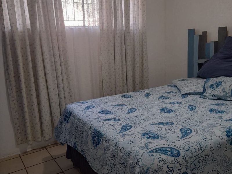 A functional bedroom featuring tiled flooring, a window with security bars, and neutral wall finishes.