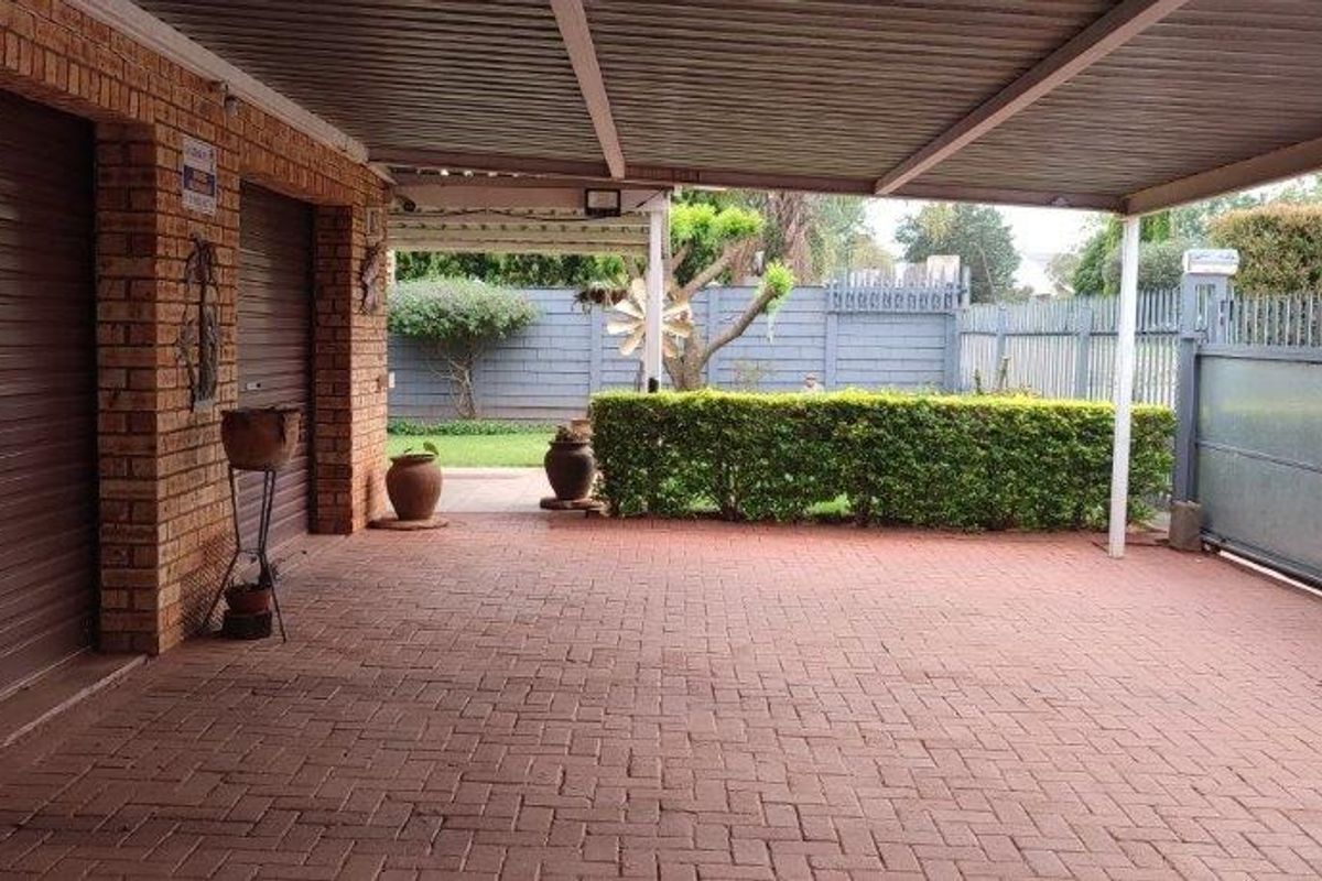 A covered carport area featuring brick paving, two roller garage doors, and a view towards the rear garden with perimeter fencing.