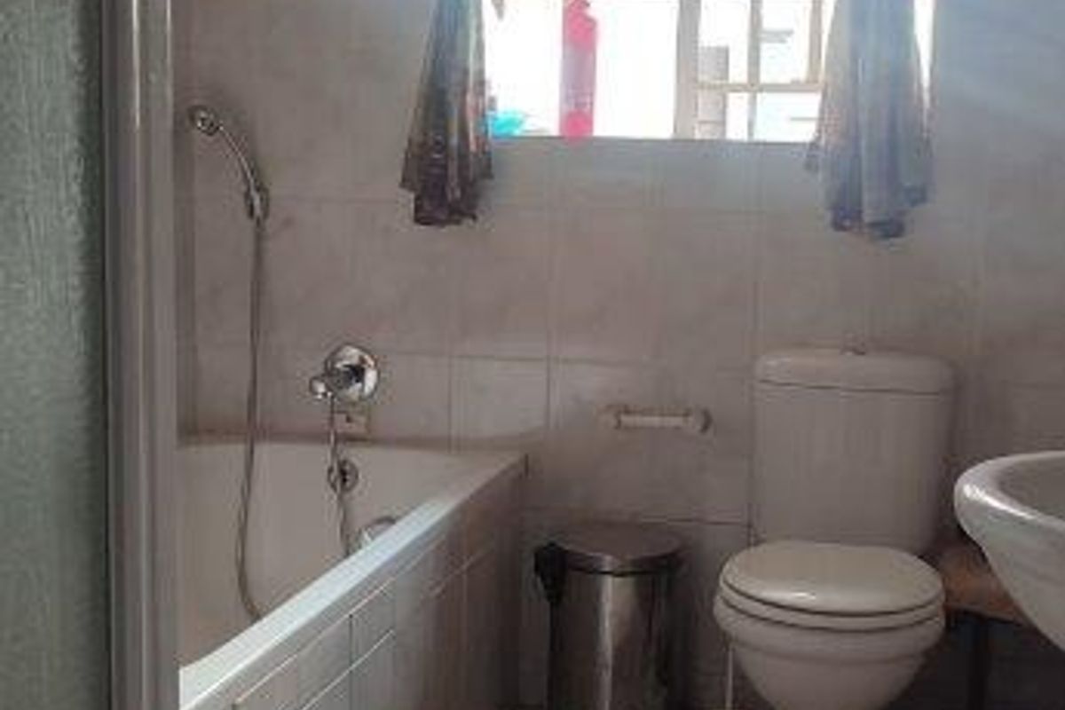 A functional bathroom featuring a built-in bathtub with shower mixer, a standard toilet, and tiled flooring.