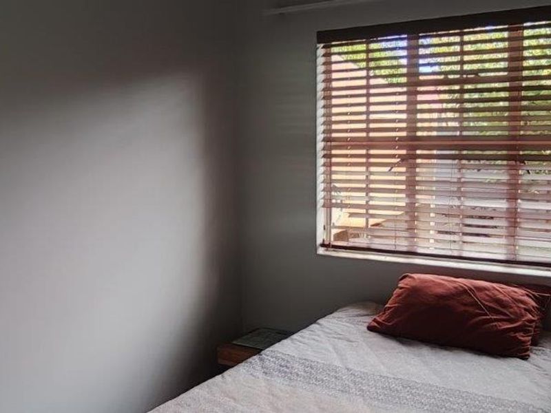 A bedroom featuring a window with fitted wooden venetian blinds, providing natural light and a view of the exterior.
