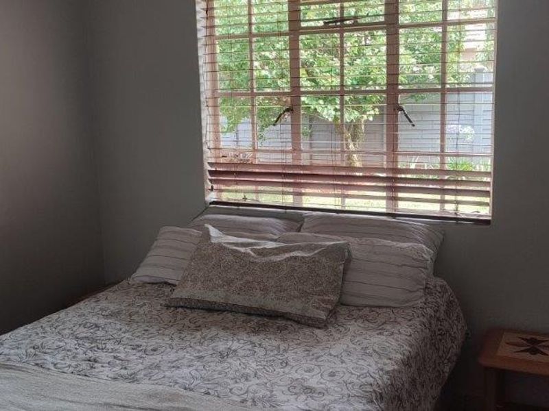 A bedroom featuring a window with fitted blinds, providing natural light and a view of the garden.