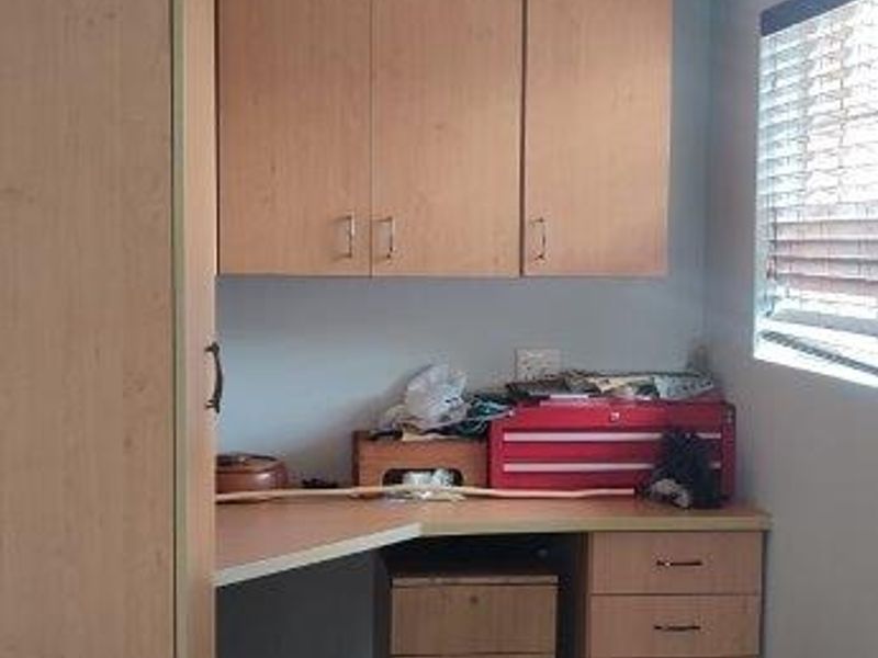 A functional home office or study area featuring built-in wooden cabinetry, desk space, and tiled flooring.