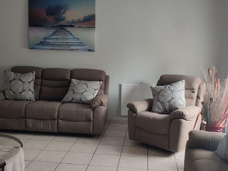 A comfortable living room featuring tiled flooring and large windows with curtains, providing a bright and inviting space for relaxation.