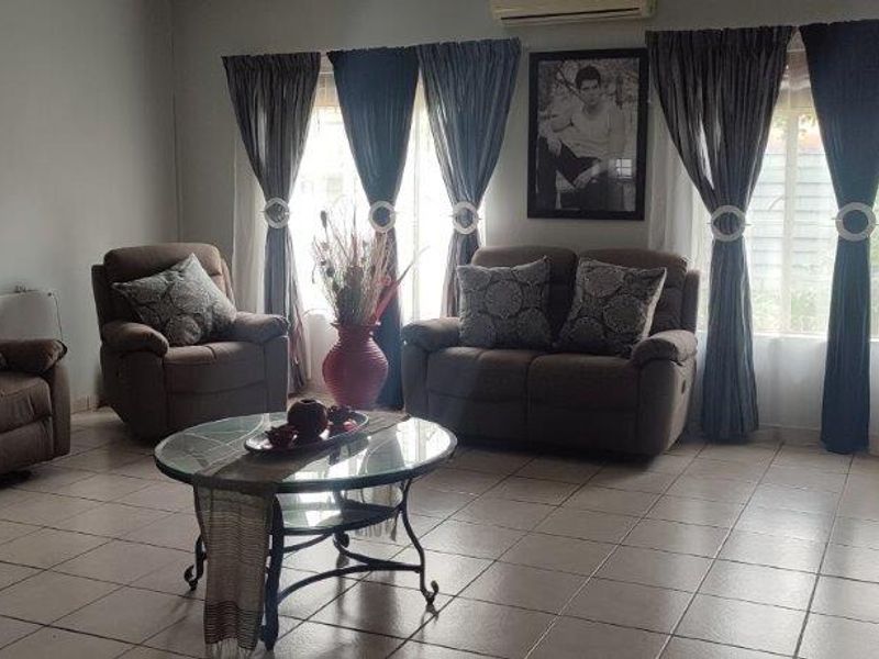 A spacious living room featuring tiled flooring, large windows with curtain treatments, and a wall-mounted air conditioning unit.