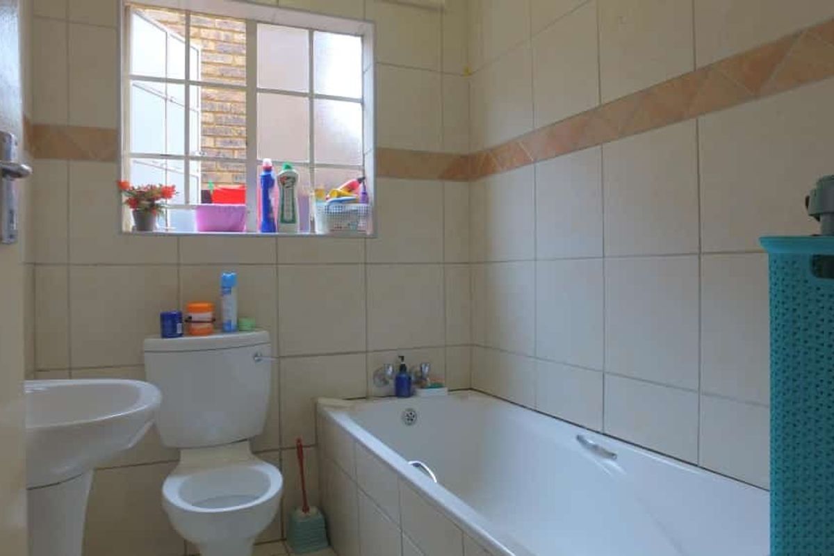 A functional bathroom featuring a standard bathtub, pedestal basin, and toilet with tiled walls and a window for natural light.