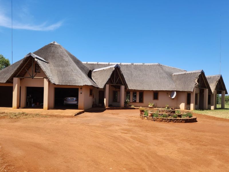 Spacious farm-style residence featuring a traditional thatched roof, integrated garage, and a circular stone-walled garden bed set within a large rural landscape.