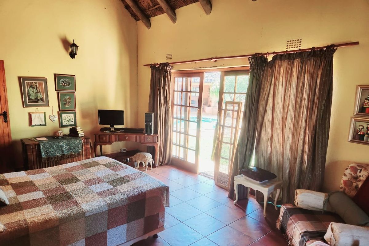 A rustic bedroom featuring a high thatched ceiling, tiled flooring, and glass sliding doors providing direct access to the outdoor pool area.