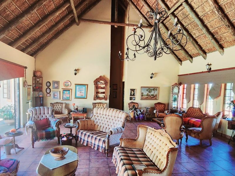 Spacious living area featuring a high vaulted thatched ceiling, exposed timber beams, terracotta floor tiles, and large windows providing natural light.