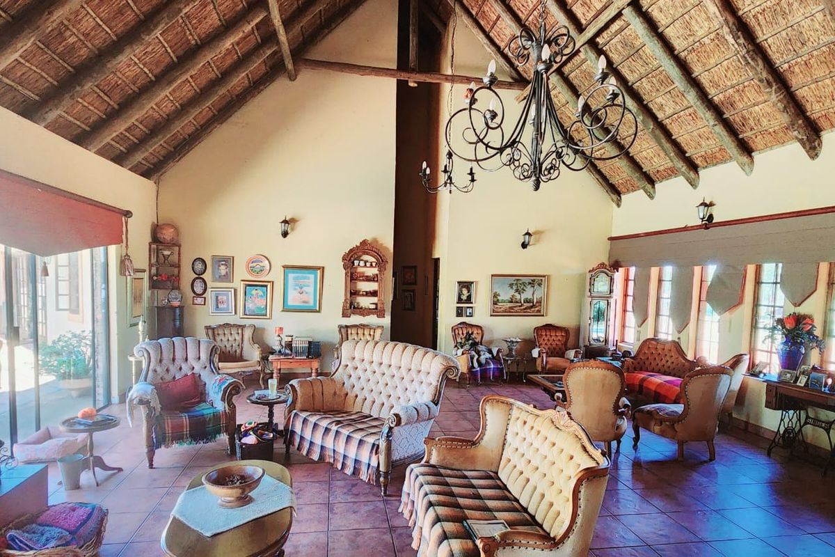Spacious living area featuring a high vaulted thatched ceiling, exposed timber beams, terracotta floor tiles, and large windows providing natural light.